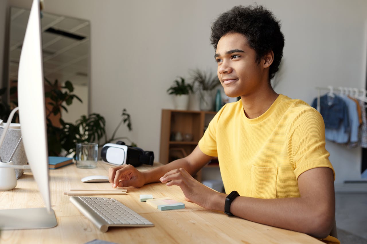 services-img Teenager smiling while studying online at home. Modern education setup with computer and VR headset.