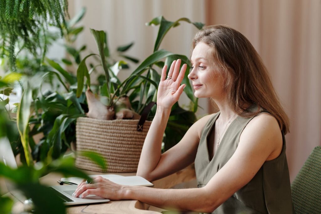 Middle-aged woman participating in a video call from a home office setting surrounded by plants.