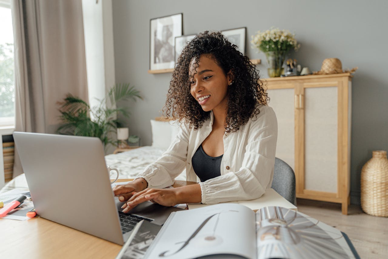 An African American woman smiling while using a laptop at a cozy home workspace.