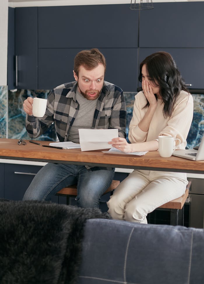 A worried couple reviewing financial documents at their kitchen table.